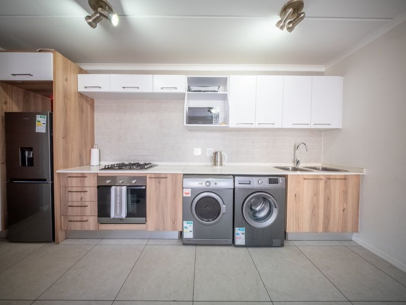 Modern kitchen featuring light wood and white cabinetry, gas hob, electric oven, double sink, and tiled flooring with integrated laundry appliance space.