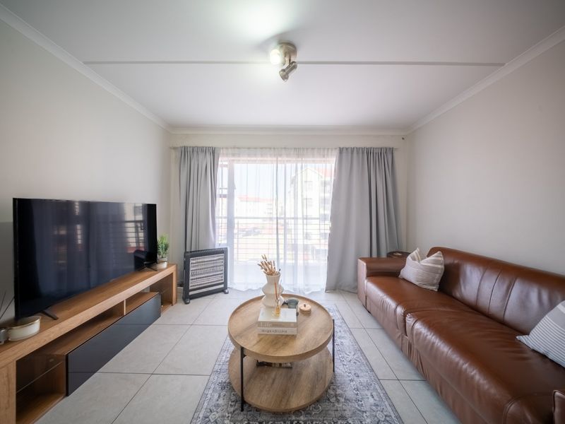 A bright and well-maintained living room featuring neutral tiled flooring, a ceiling spotlight, and a large sliding glass door providing natural light.