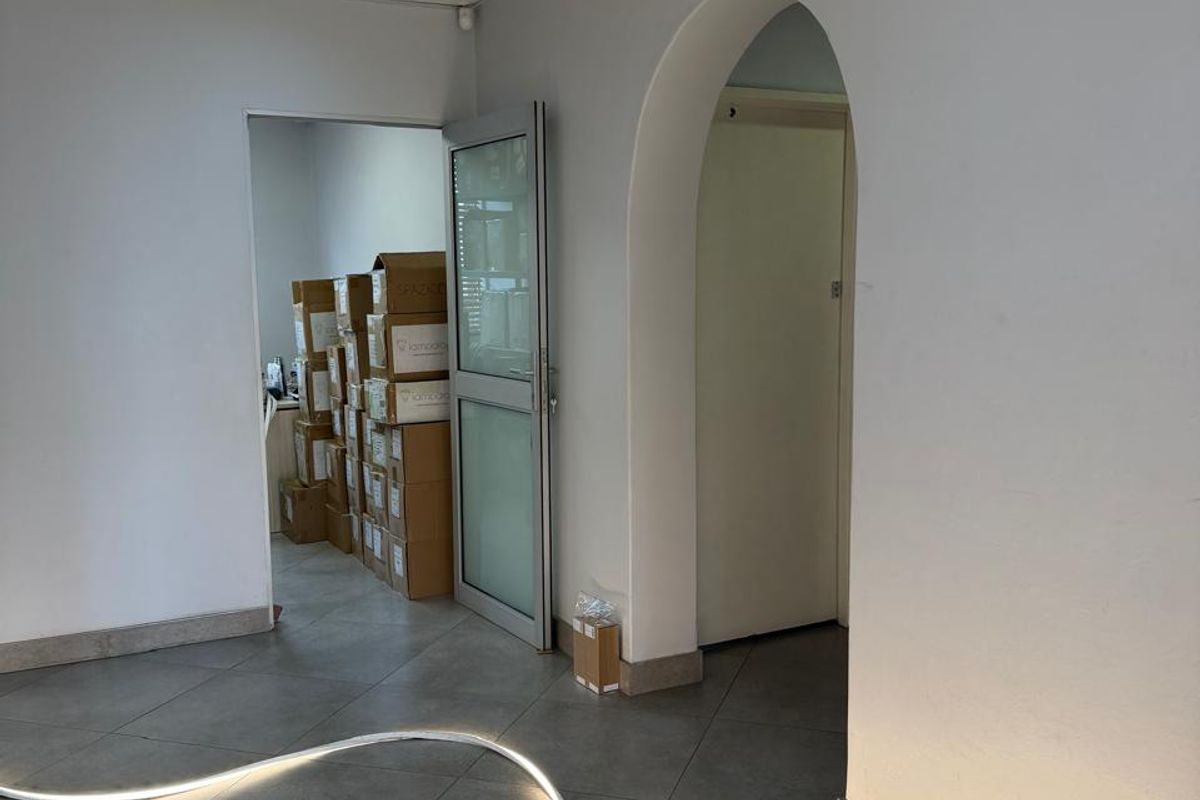 A commercial hallway featuring tiled flooring, a suspended ceiling, and an arched doorway leading to adjacent office or storage spaces.