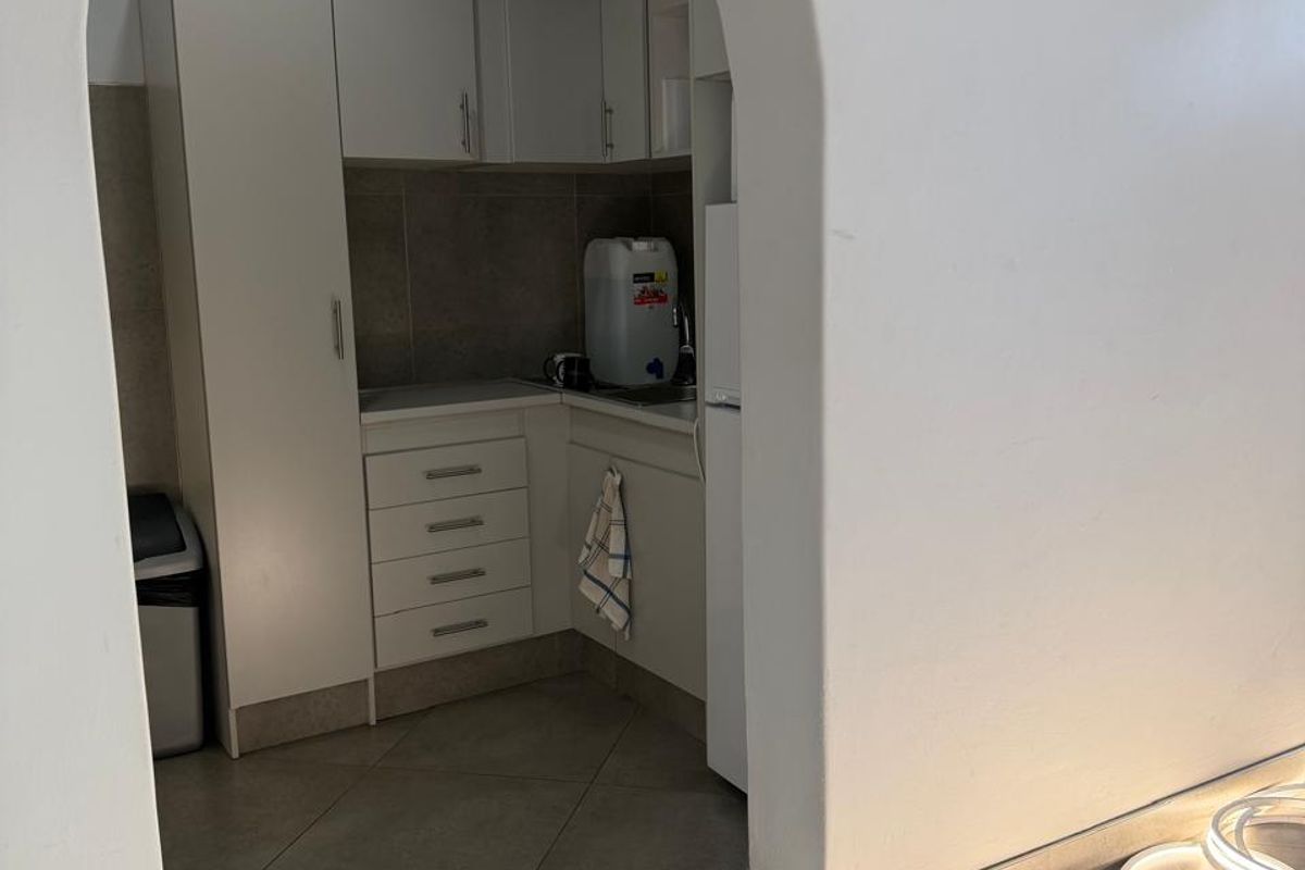 A compact kitchenette featuring built-in white cabinetry, tiled flooring, and a functional sink area, accessed through a distinctive arched doorway.