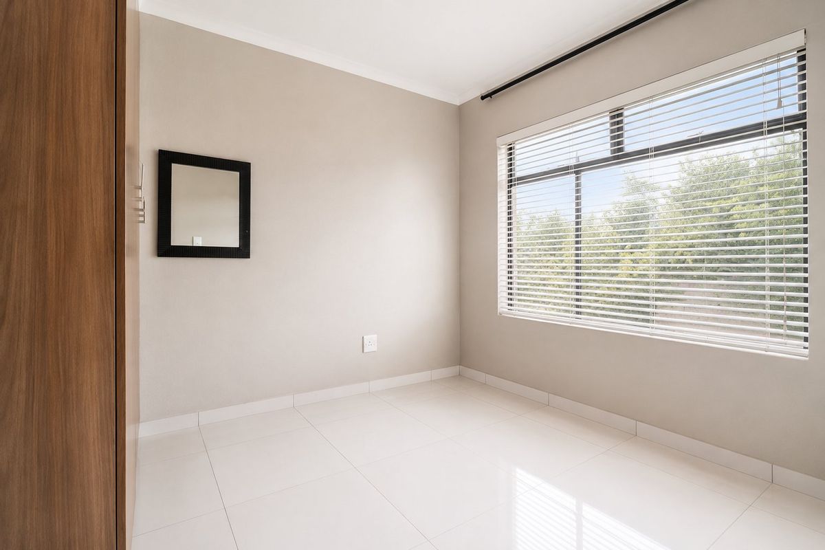 A bright, empty bedroom featuring neutral wall tones, large white floor tiles, and a window fitted with horizontal blinds.