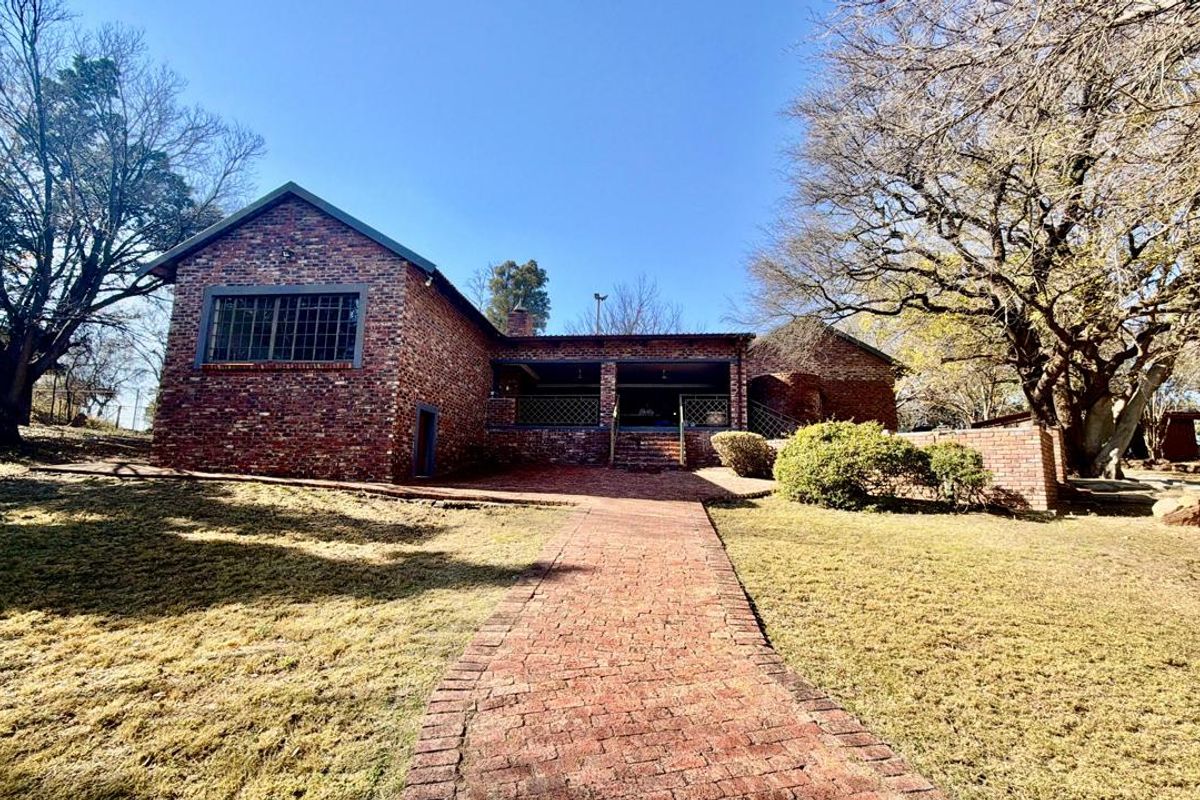 A rear view of a brick house featuring a covered patio, a brick paved walkway, and established garden surroundings.
