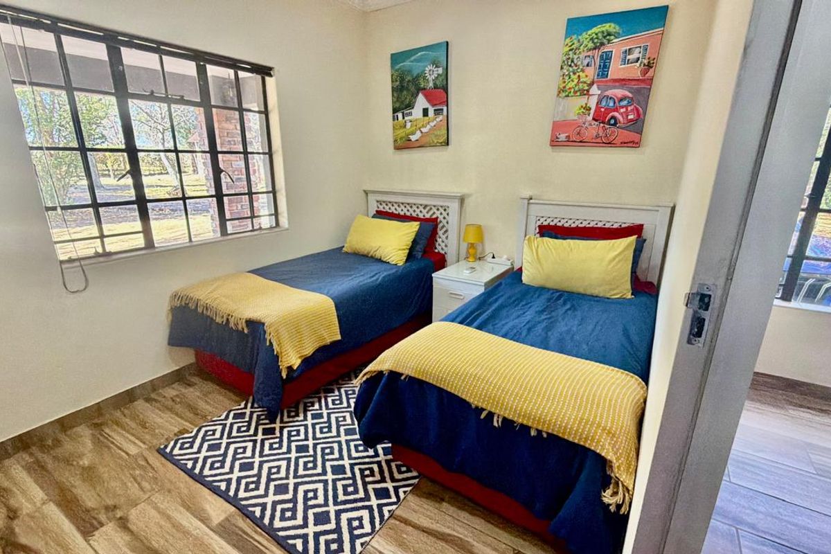 A functional bedroom featuring wood-look tile flooring and large steel-framed windows providing natural light.