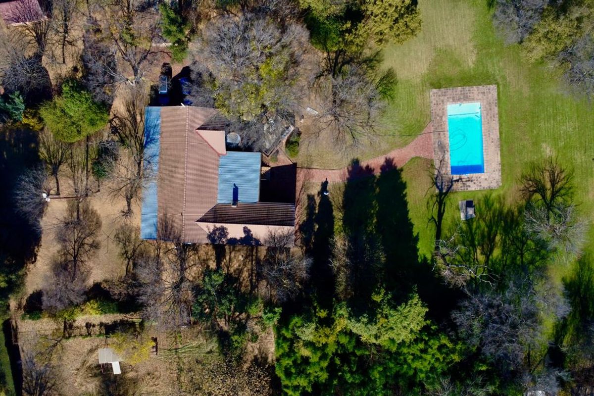 Aerial view of the property showcasing the main dwelling, a swimming pool with paved surround, and extensive landscaped garden grounds.