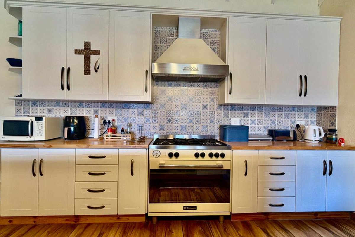 A well-maintained kitchen featuring white shaker-style cabinetry, wooden countertops, a gas stove with an extractor fan, and a decorative patterned tile backsplash.