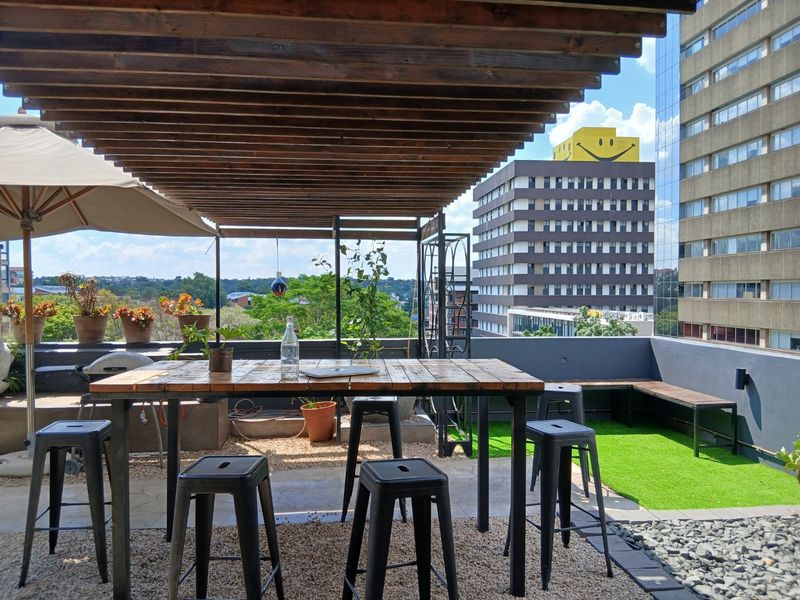 Spacious rooftop balcony featuring a timber pergola, built-in bench seating, and artificial grass, offering an elevated outdoor entertainment area with urban views.