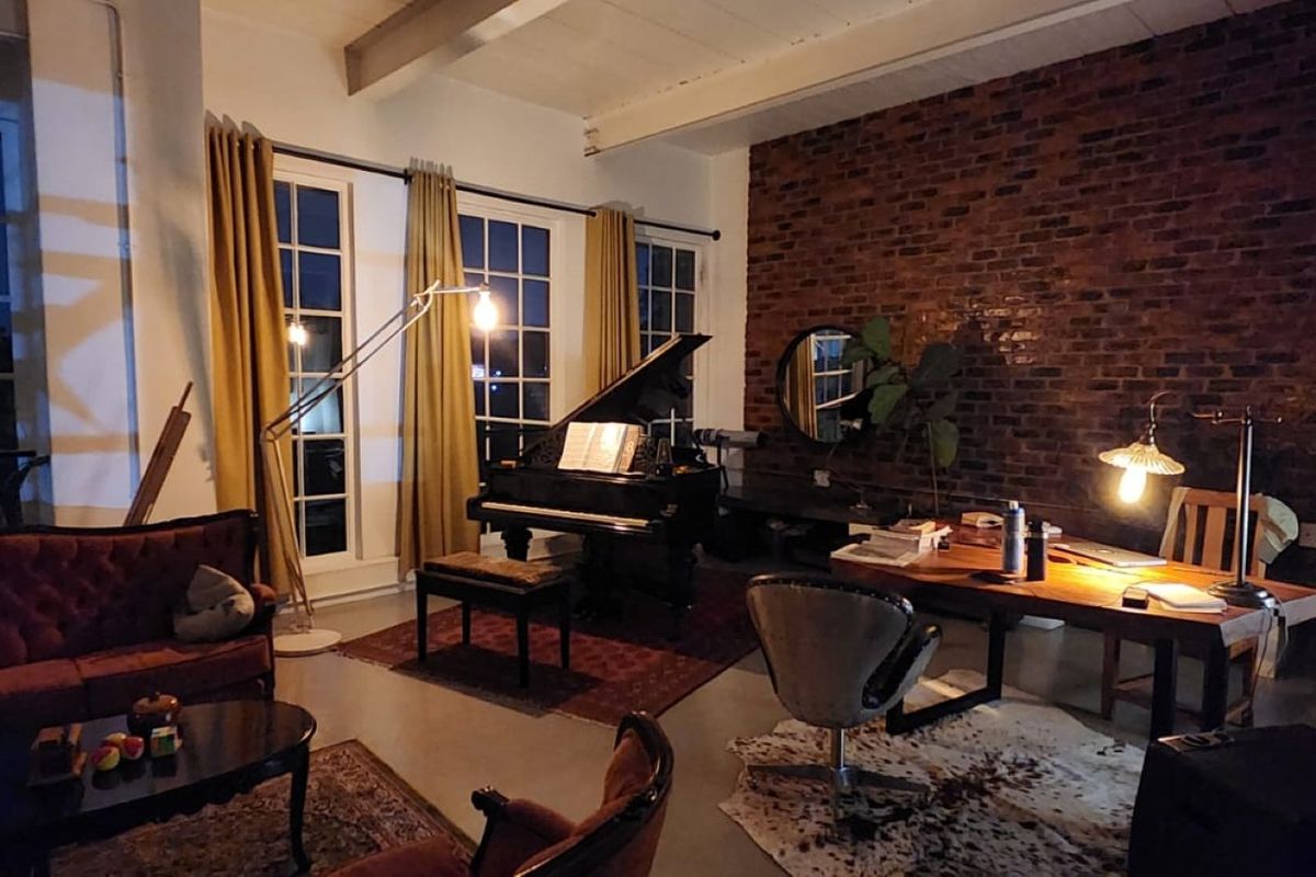 Spacious living area featuring an exposed brick feature wall, high ceilings with exposed beams, and large windows providing ample natural light.