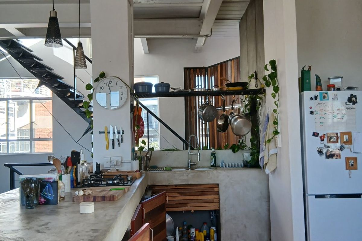Industrial-style kitchen featuring concrete countertops, exposed ceiling beams, a gas hob, and an open-concept layout with an adjacent staircase.
