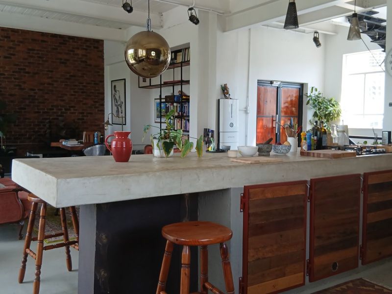 Spacious open-plan living area featuring a large concrete kitchen island, exposed brick wall, and industrial-style architectural elements.