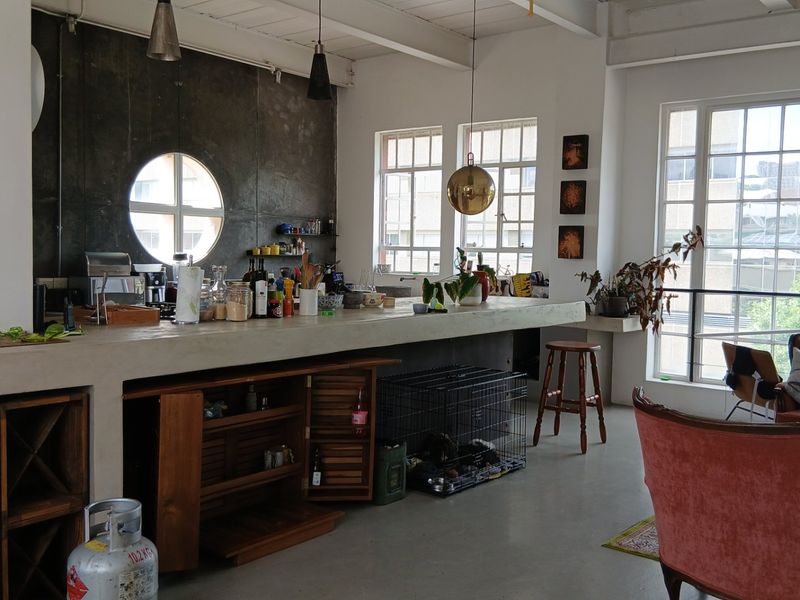 Spacious open-plan living area featuring a large concrete kitchen island, exposed ceiling beams, and large multi-pane windows providing ample natural light.