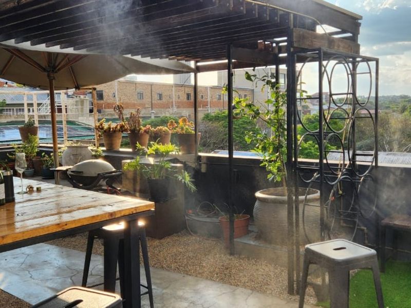 An elevated rooftop patio featuring a timber pergola, metal framing, and a mix of gravel and artificial grass flooring with urban views.