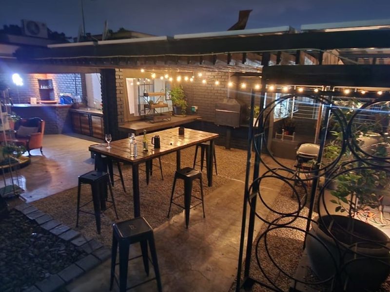 A covered outdoor patio area featuring exposed brick walls, a built-in braai, and ambient string lighting, ideal for evening entertainment.