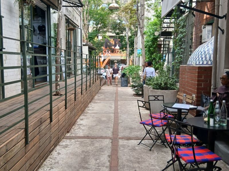 An outdoor pedestrian walkway featuring timber decking, metal railings, and commercial awnings, creating a vibrant urban atmosphere between building facades.