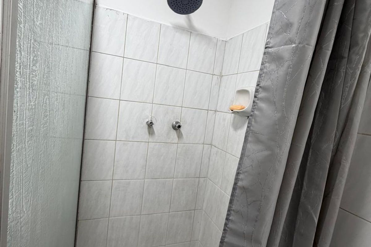 A functional shower enclosure featuring white wall tiles, a mosaic tiled floor, and a modern black shower head.