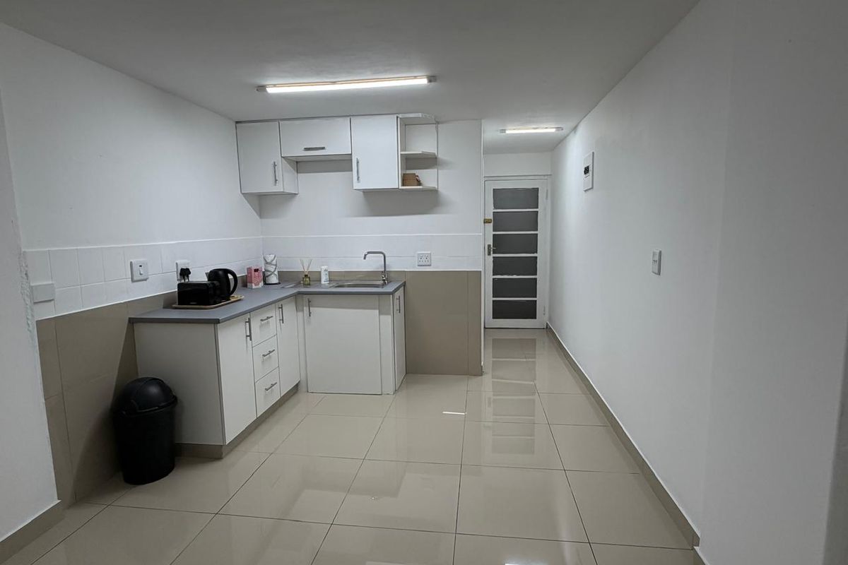 A functional kitchen featuring white built-in cabinetry, laminate countertops, a stainless steel sink, and neutral tiled flooring with a tiled backsplash.