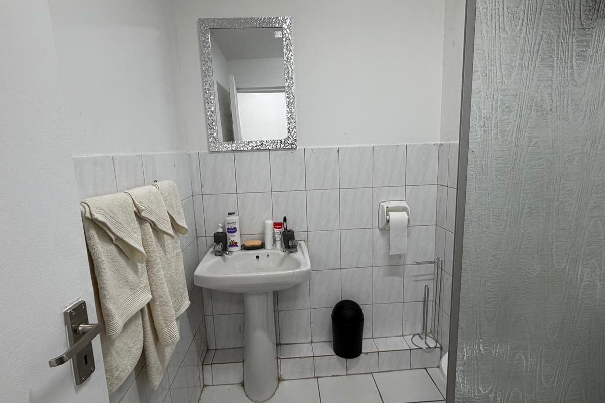 A compact bathroom featuring a pedestal basin, tiled walls and flooring, and a shower screen, requiring some maintenance and cosmetic updates.
