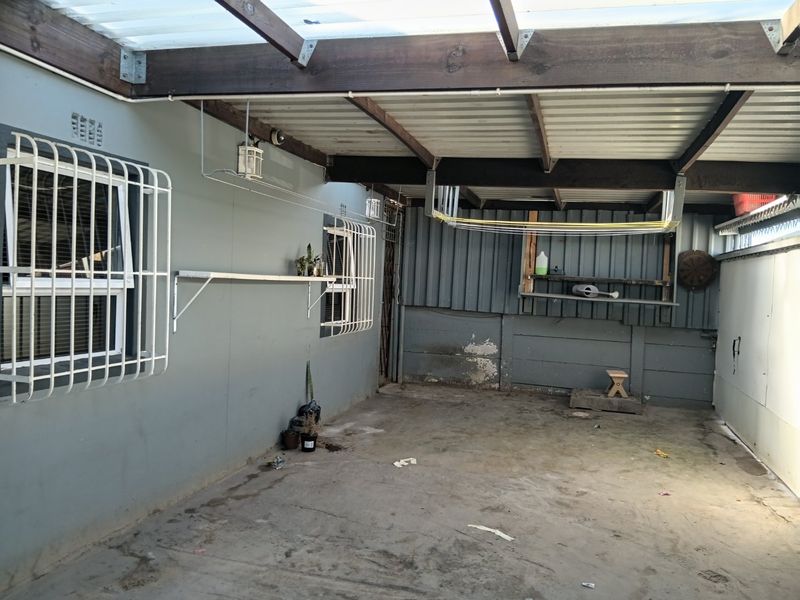 A covered outdoor patio area featuring concrete flooring, security bars on windows, and a timber-framed roof structure with a wall-mounted drying rack.