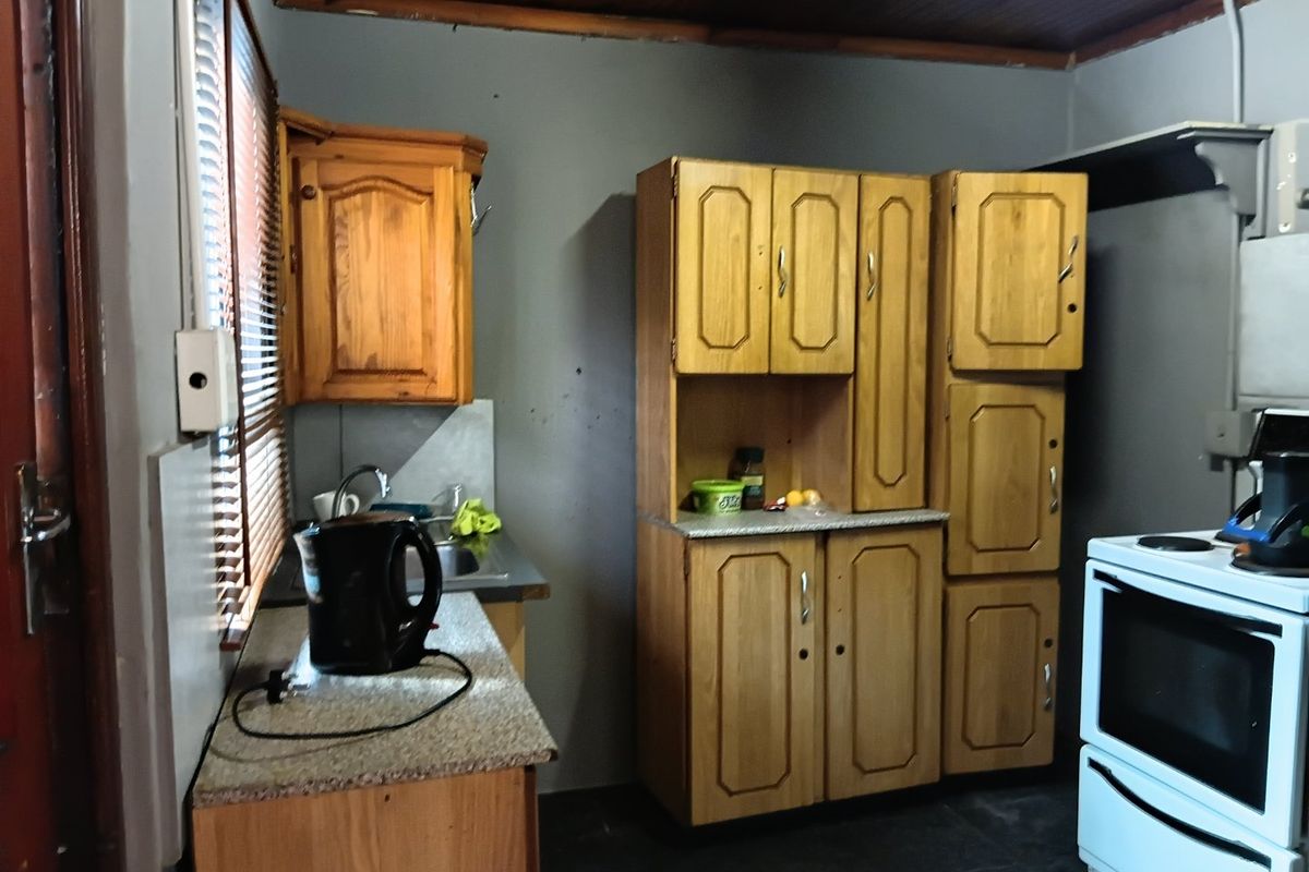 A compact kitchen featuring wooden cabinetry, laminate countertops, a stainless steel sink, and a freestanding oven, with a timber-paneled ceiling.