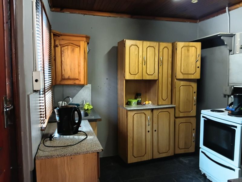 A compact kitchen featuring wooden cabinetry, laminate countertops, a stainless steel sink, and a freestanding oven, with a timber-paneled ceiling.