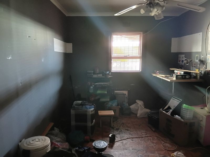 A bedroom featuring a ceiling fan and window with blinds, currently requiring significant cosmetic repairs to the walls and flooring.