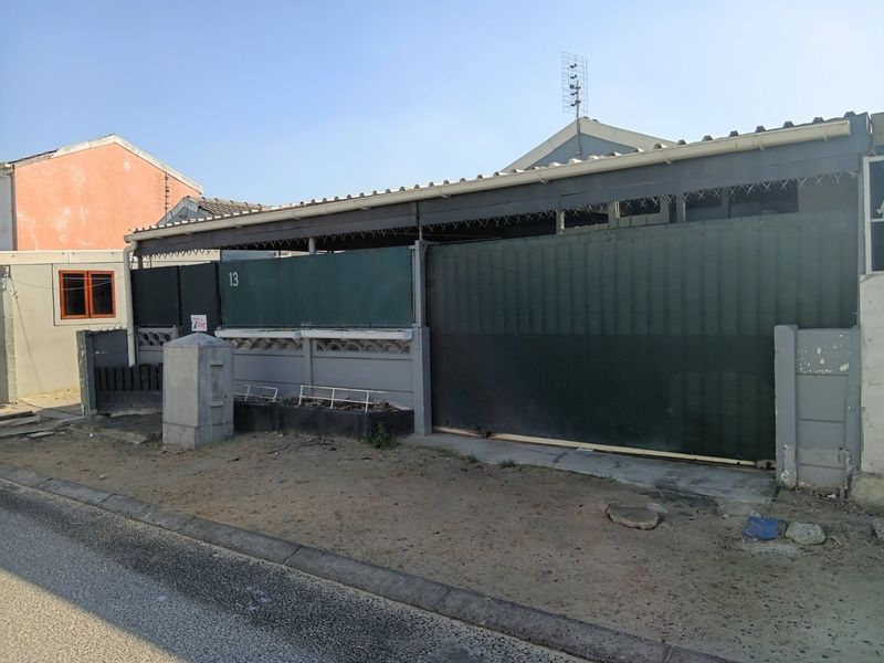 Front exterior view of the property featuring a sliding gate, perimeter wall, and roof structure.