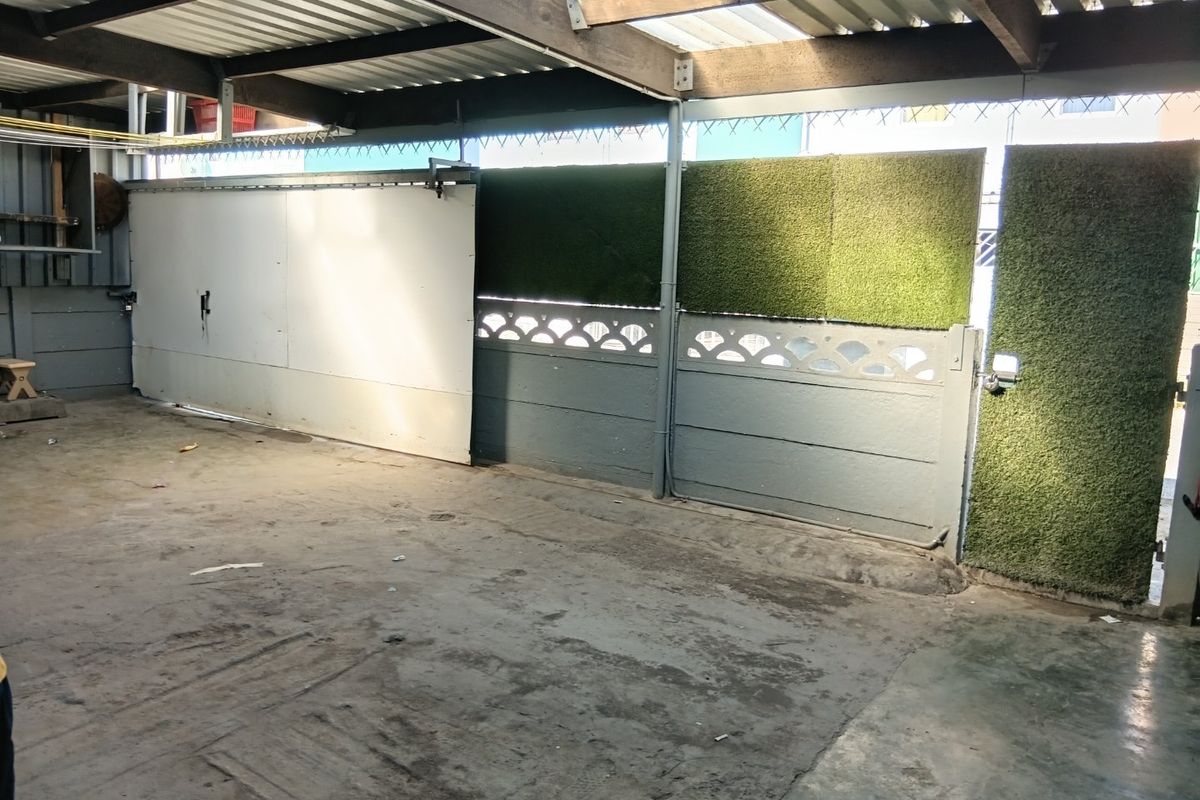 A functional garage space featuring a corrugated roof, concrete flooring, and a sliding gate entrance with decorative precast walling.