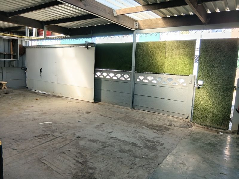A functional garage space featuring a corrugated roof, concrete flooring, and a sliding gate entrance with decorative precast walling.