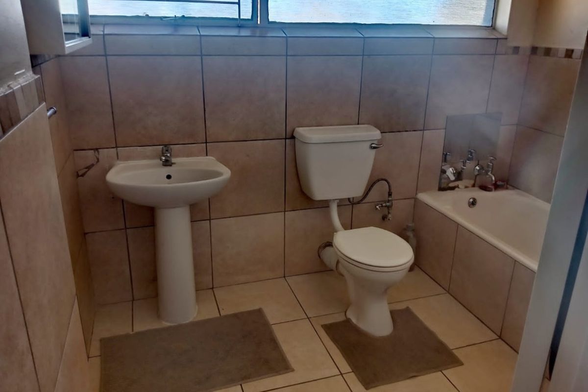 A functional bathroom featuring a pedestal basin, toilet, and built-in bathtub with tiled finishes throughout.