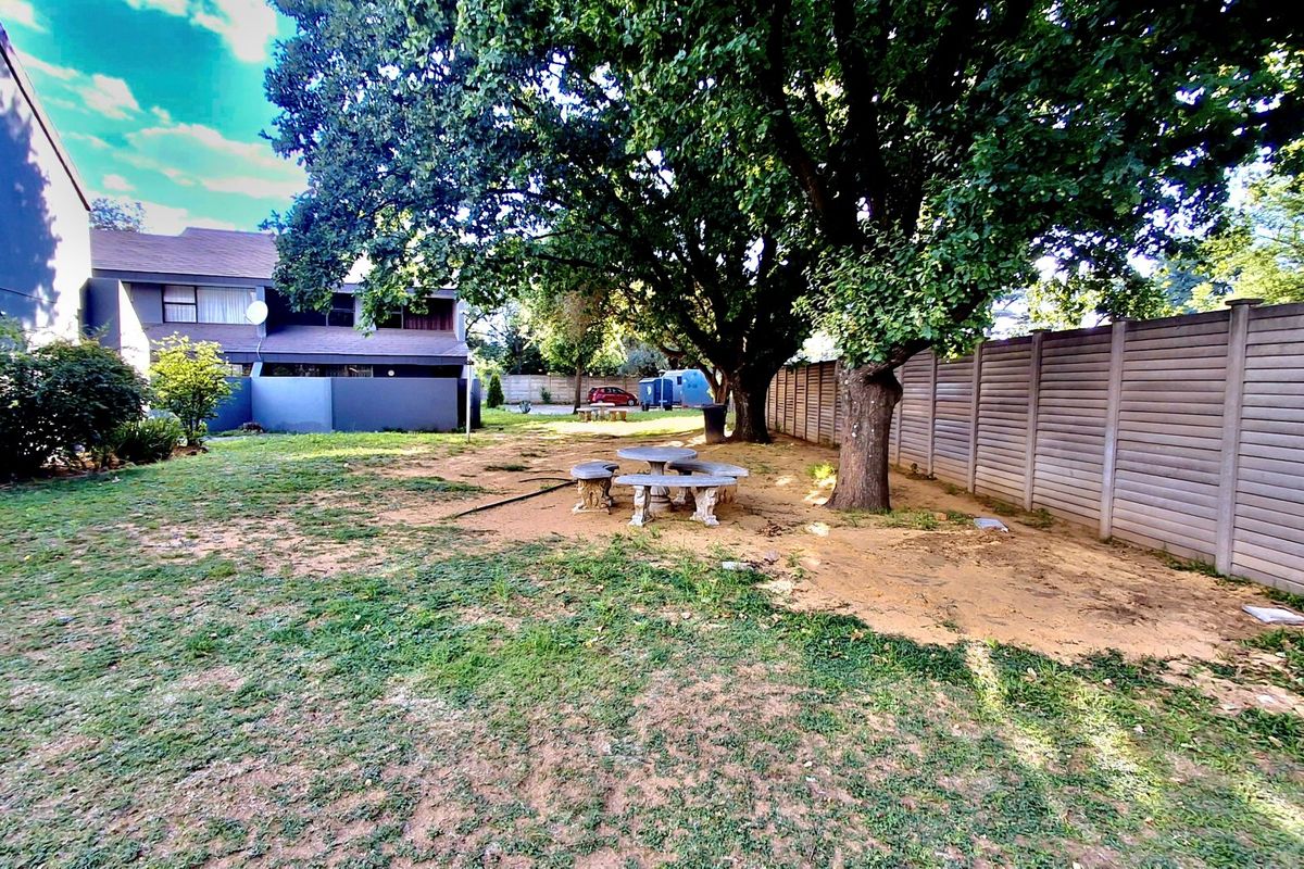 A spacious rear garden area featuring mature trees, a precast concrete boundary wall, and an open lawn space with potential for landscaping.