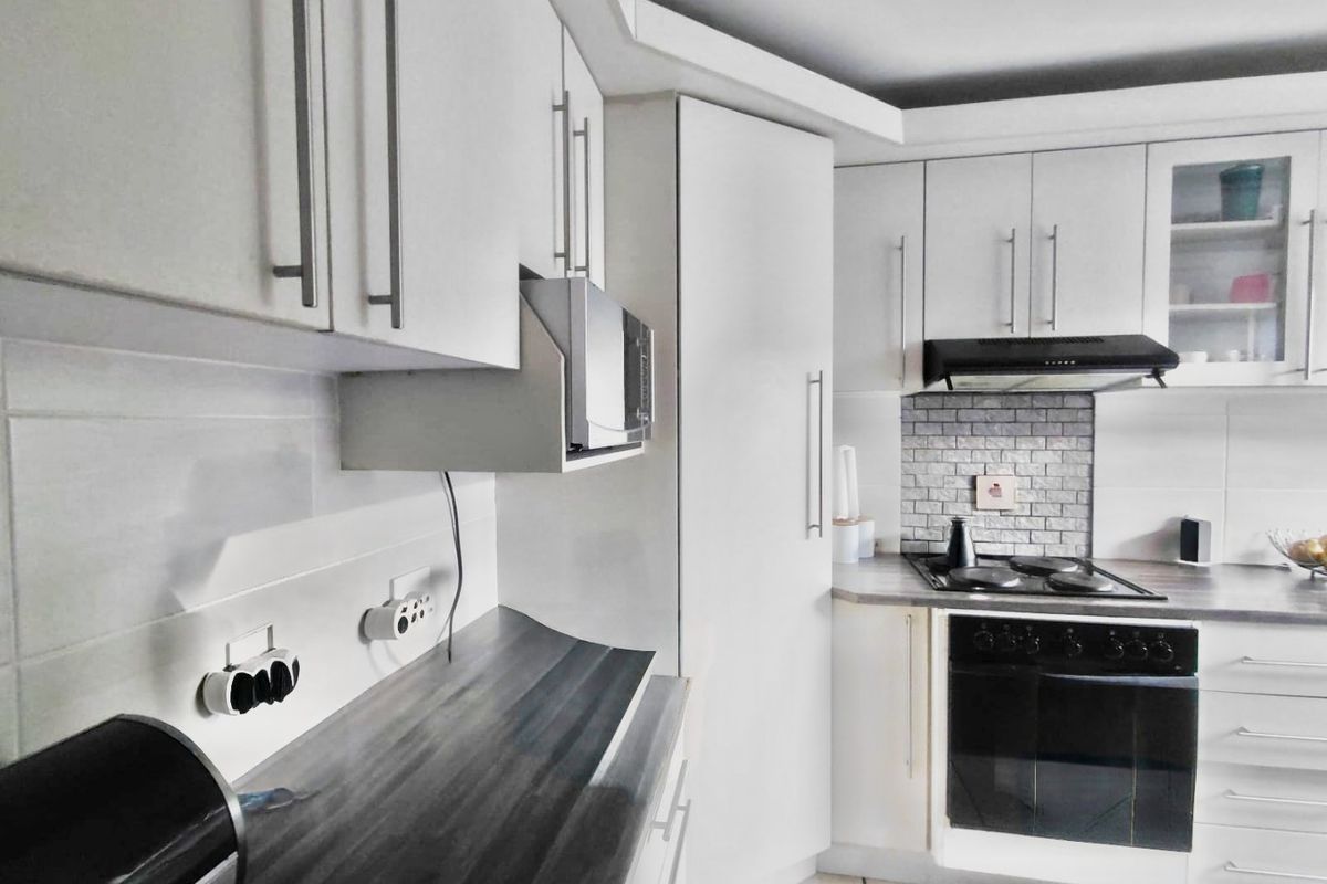 A functional kitchen featuring white cabinetry, dark laminate countertops, a built-in oven with gas hob, and a tiled backsplash.