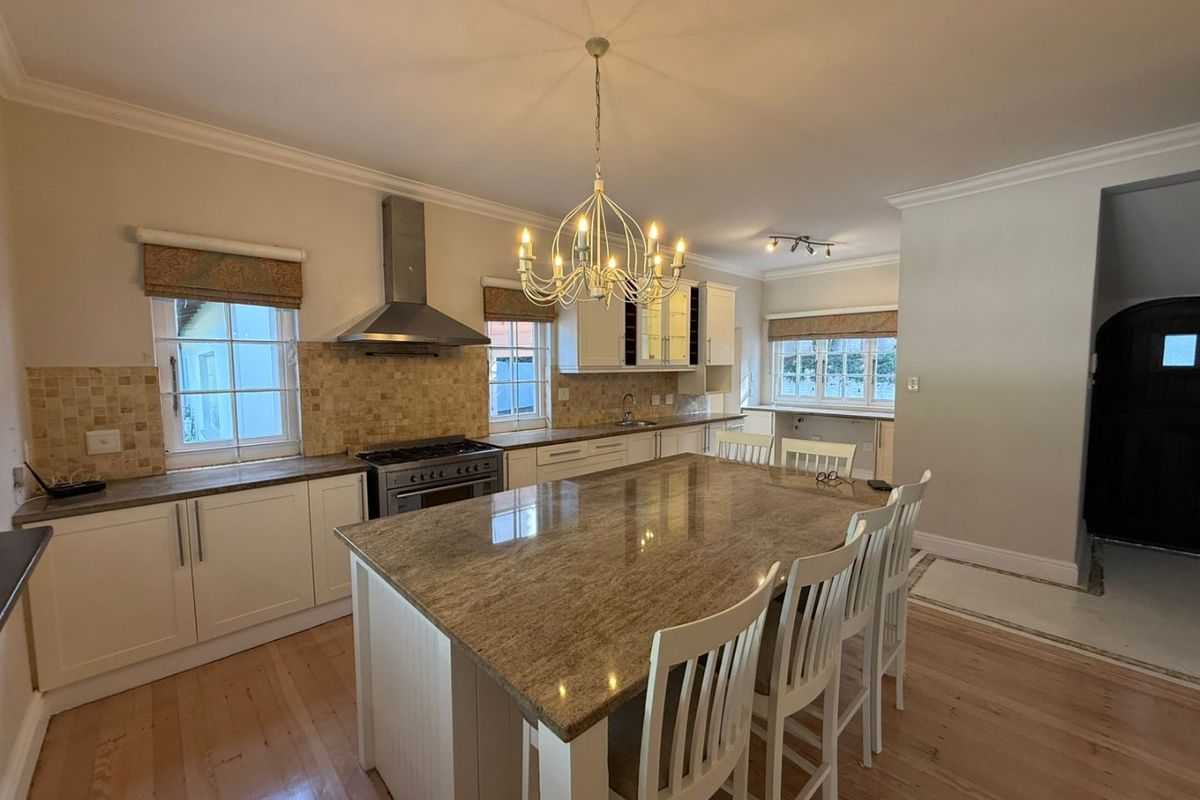 Spacious kitchen featuring a large granite-topped island, stainless steel extractor fan, gas stove, and ample built-in cabinetry with hardwood flooring.