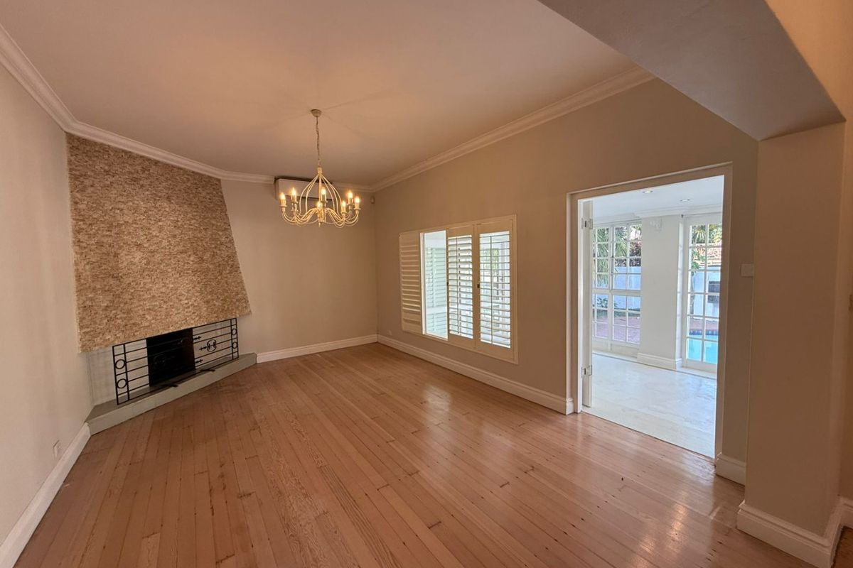 Spacious living room featuring polished hardwood floors, a distinctive stone-clad fireplace, and plantation shutters, with direct access to an adjoining sunroom.