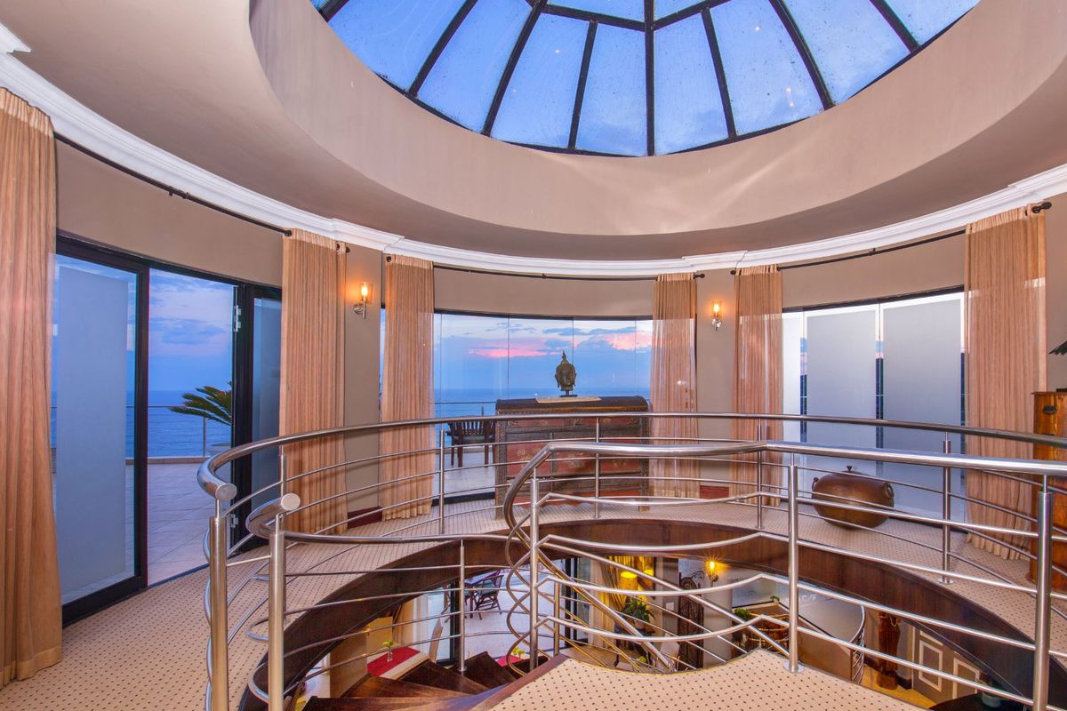 A unique circular living space featuring a central spiral staircase, a dramatic domed skylight, and expansive curved windows offering panoramic ocean views.