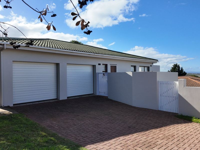 Front view of the property featuring a double garage, paved driveway, and secure boundary wall with pedestrian access.