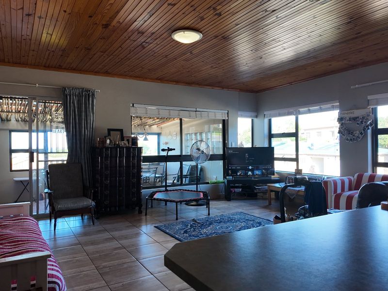 Spacious living area featuring a warm timber tongue and groove ceiling, tiled flooring, and large windows that provide ample natural light.