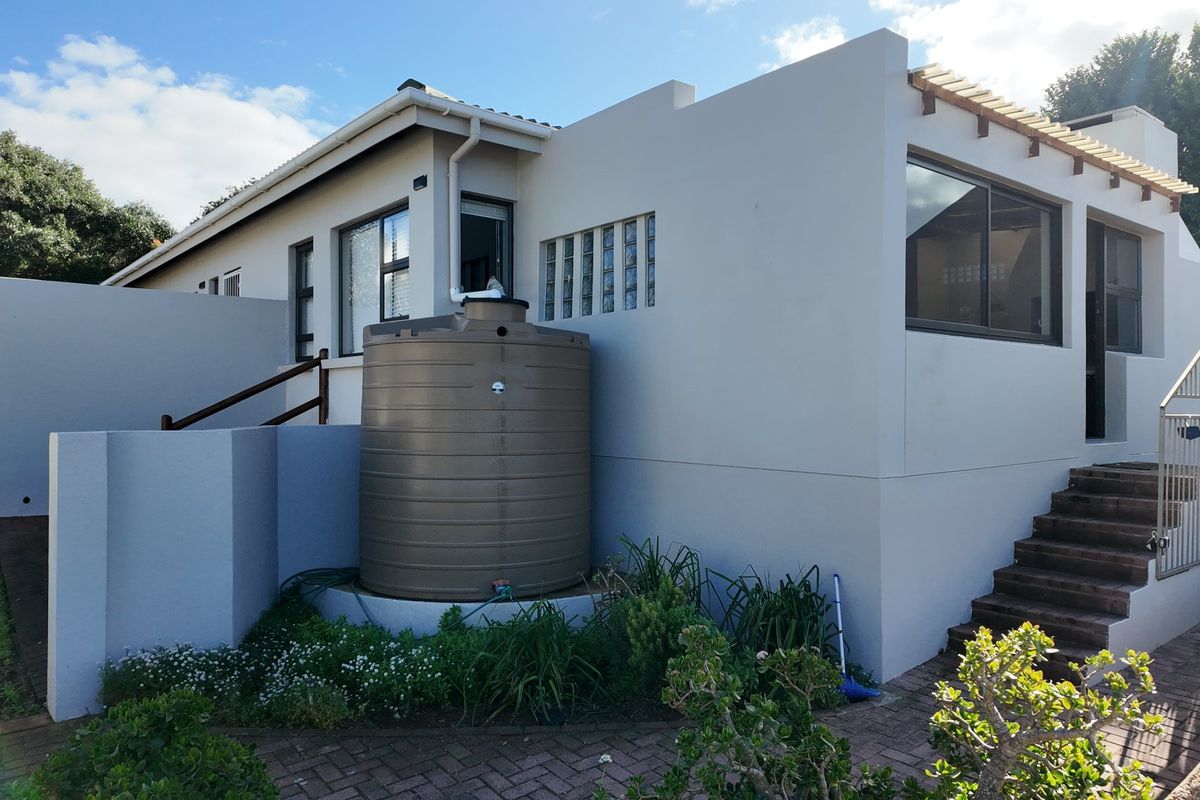 Rear exterior view of the property featuring a paved patio, external staircase, timber pergola, and a large water storage tank.