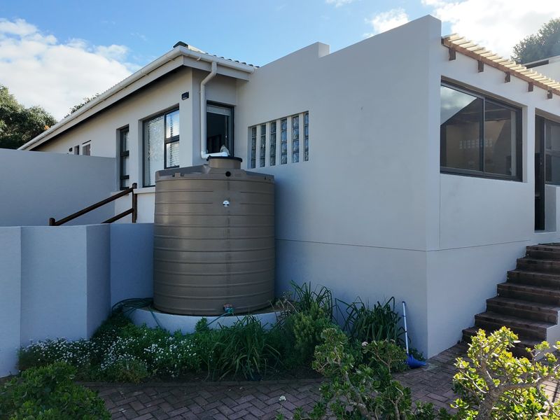 Rear exterior view of the property featuring a paved patio, external staircase, timber pergola, and a large water storage tank.