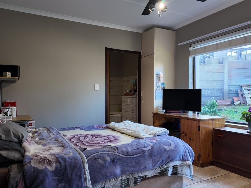 A functional bedroom featuring tiled flooring, a built-in cupboard, and a ceiling fan, with direct access to an en-suite bathroom.