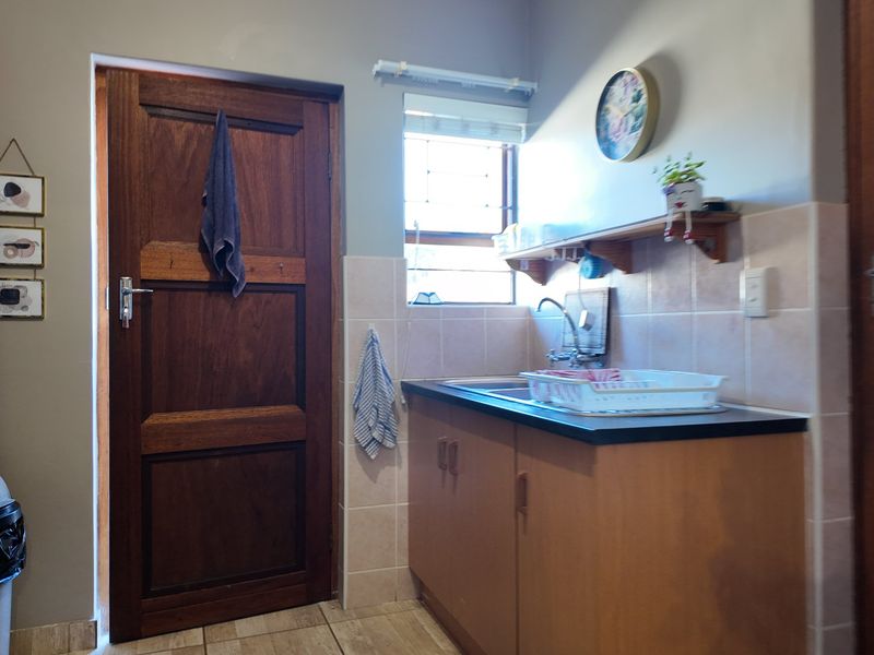 A functional laundry area featuring built-in cabinetry, a sink with tiled splashback, and classic timber doors.