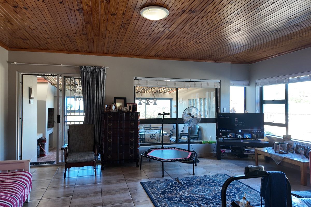 Spacious living room featuring a warm timber tongue and groove ceiling, tiled flooring, and large windows providing ample natural light and access to the patio.