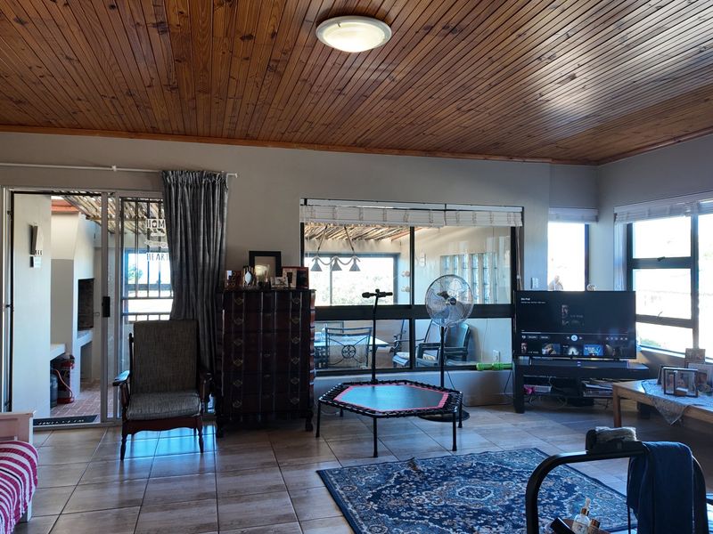 Spacious living room featuring a warm timber tongue and groove ceiling, tiled flooring, and large windows providing ample natural light and access to the patio.