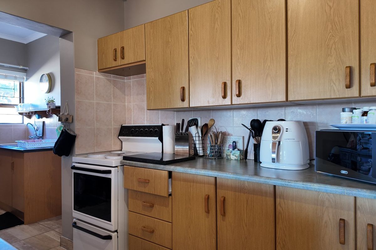 A functional kitchen featuring wood-look laminate cabinetry, tiled backsplash, and a freestanding stove, with an adjacent scullery area visible through the doorway.