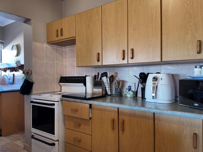 A functional kitchen featuring wood-look laminate cabinetry, tiled backsplash, and a freestanding stove, with an adjacent scullery area visible through the doorway.