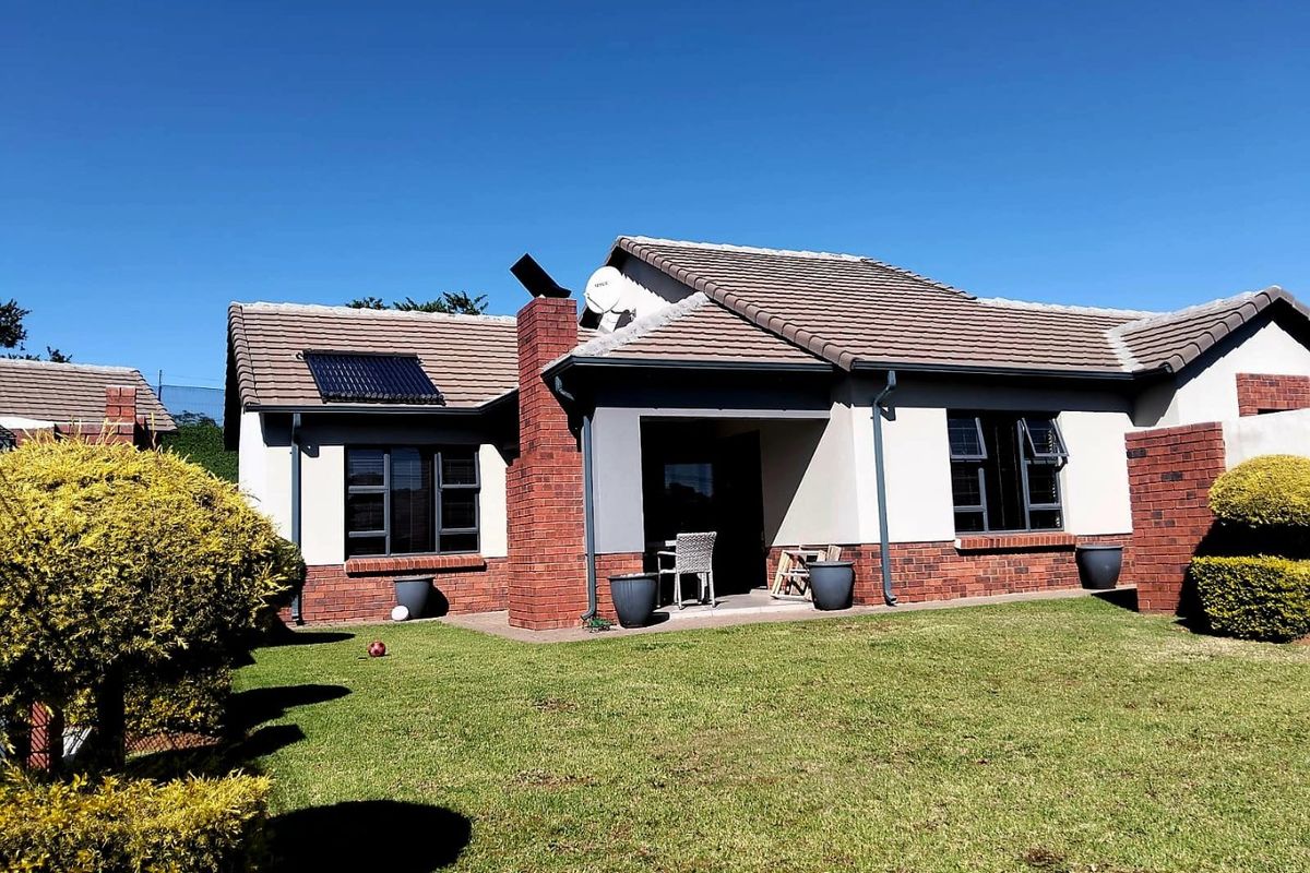 Rear view of the townhouse featuring a tiled roof, brick chimney, solar water heating panel, and a covered patio overlooking the garden.