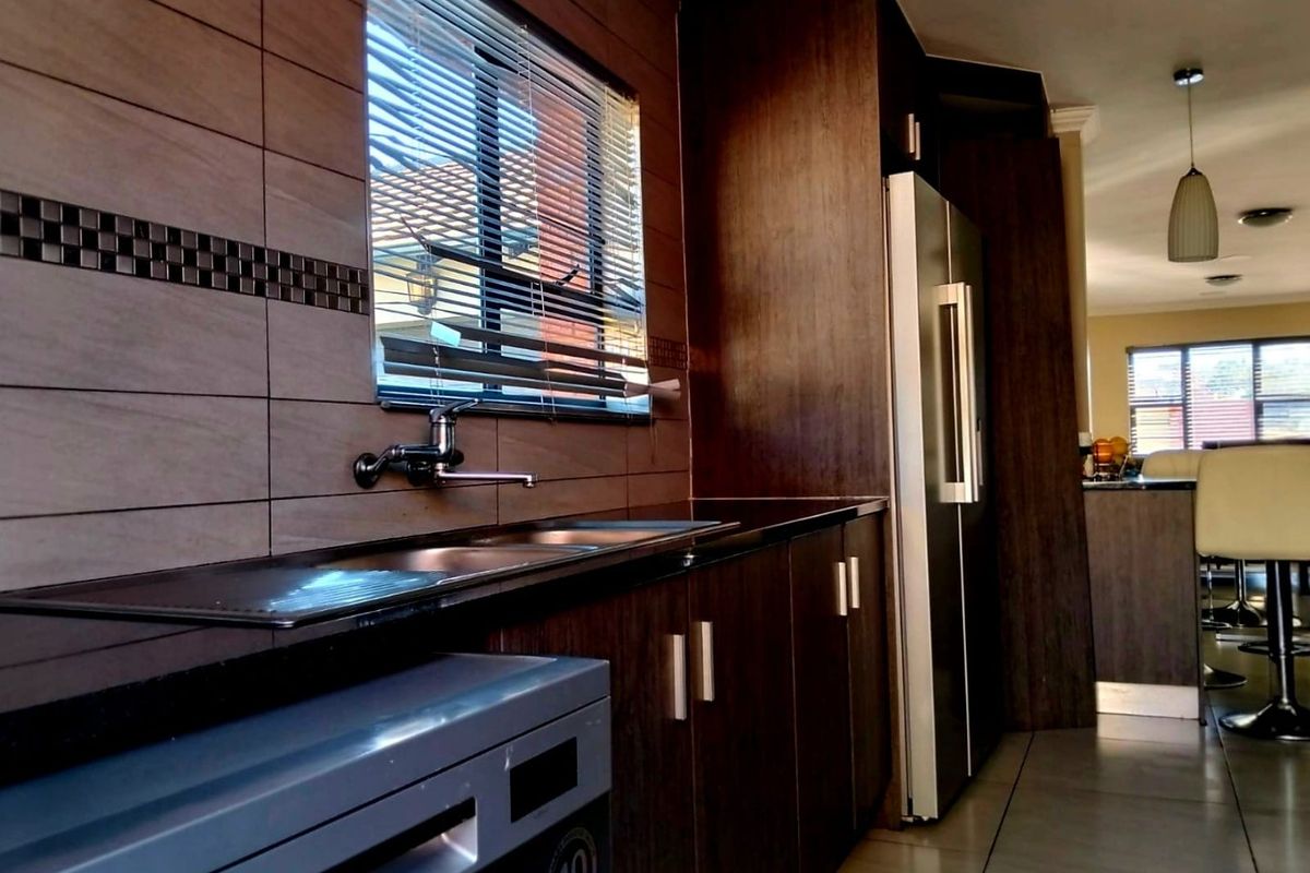 Modern kitchen featuring dark wood cabinetry, sleek black granite countertops, a stainless steel double sink, and stylish tiled splashbacks.