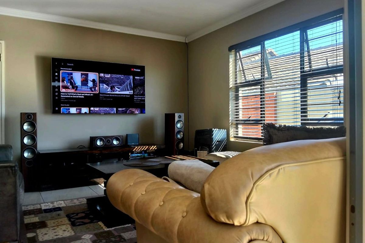 A comfortable living room featuring tiled flooring, recessed ceiling lighting, and large windows with fitted venetian blinds.