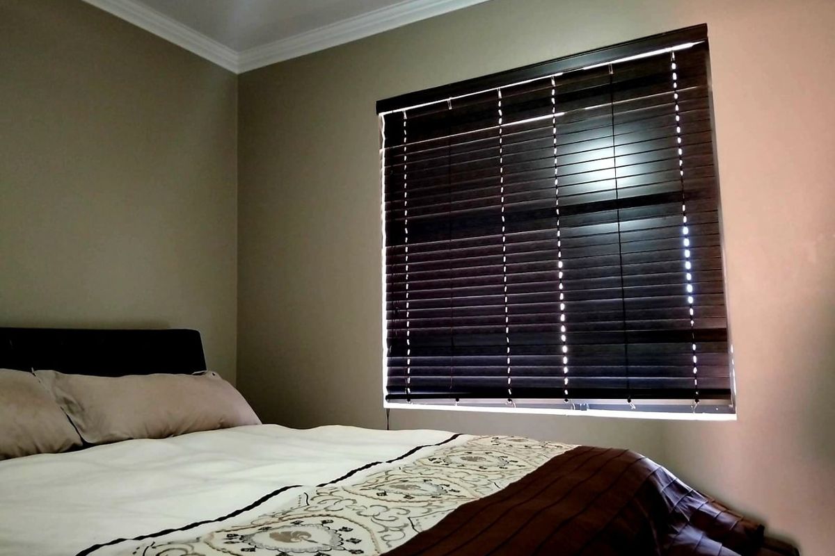 A cozy bedroom featuring neutral wall tones, decorative ceiling cornicing, and dark venetian blinds for adjustable natural light control.