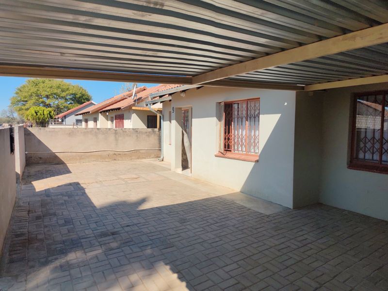 Front exterior view featuring a paved driveway, covered carport, and secure window grilles on the building facade.