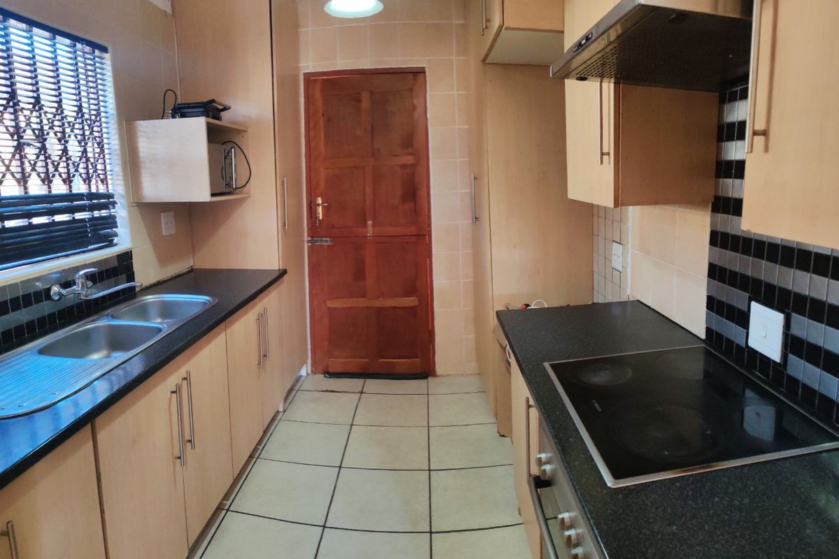 Functional galley-style kitchen featuring laminate cabinetry, black granite countertops, integrated electric hob, oven, and extractor fan with tiled flooring and backsplash.