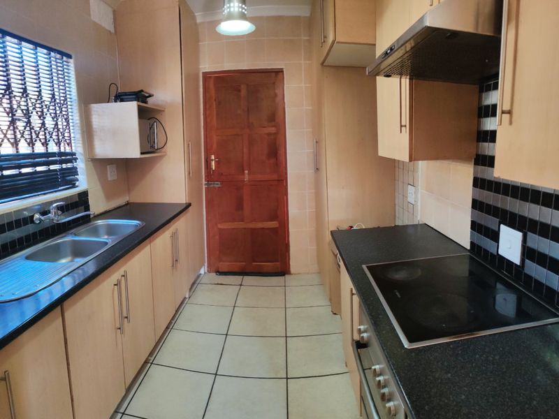 Functional galley-style kitchen featuring laminate cabinetry, black granite countertops, integrated electric hob, oven, and extractor fan with tiled flooring and backsplash.